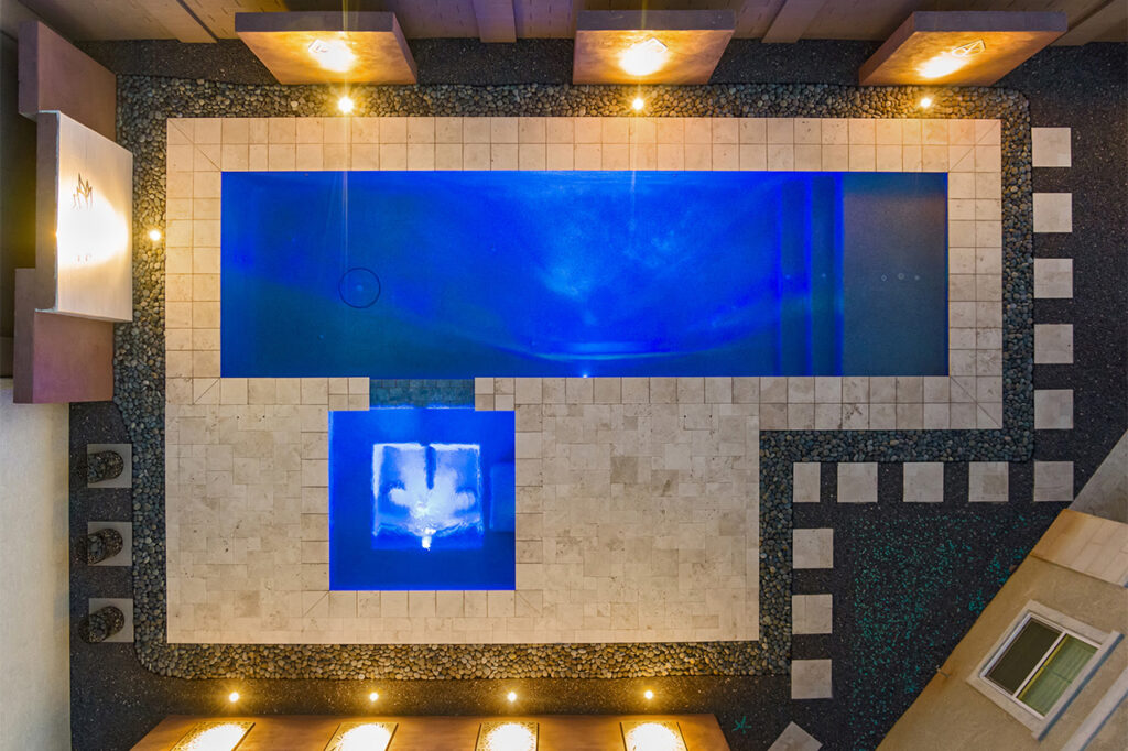 Modern Phoenix backyard pool with travertine tile decking, illuminated water feature, and geometric landscaping.