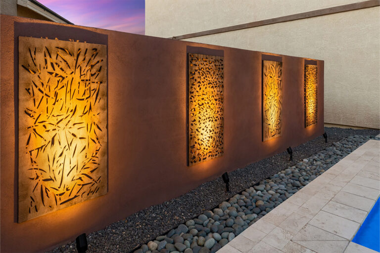 Lit decorative metal wall panels above river rock landscaping