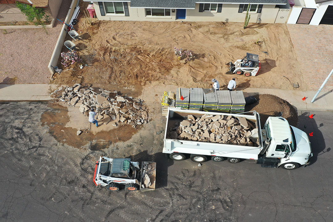 Crew preparing a Phoenix front yard for paver installation with heavy equipment and demolition debris.
