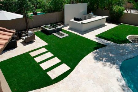 Modern Phoenix backyard with synthetic grass, travertine pavers, and an outdoor kitchen next to a swimming pool.
