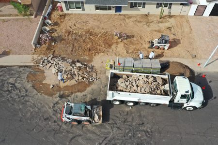 Crew preparing a Phoenix front yard for paver installation with heavy equipment and demolition debris.